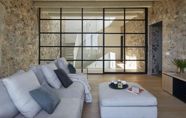 Can Torredà | Salón con sofá y amplio ventanal que permite ver la escalera interior | Damian Ribas | Alumilux
